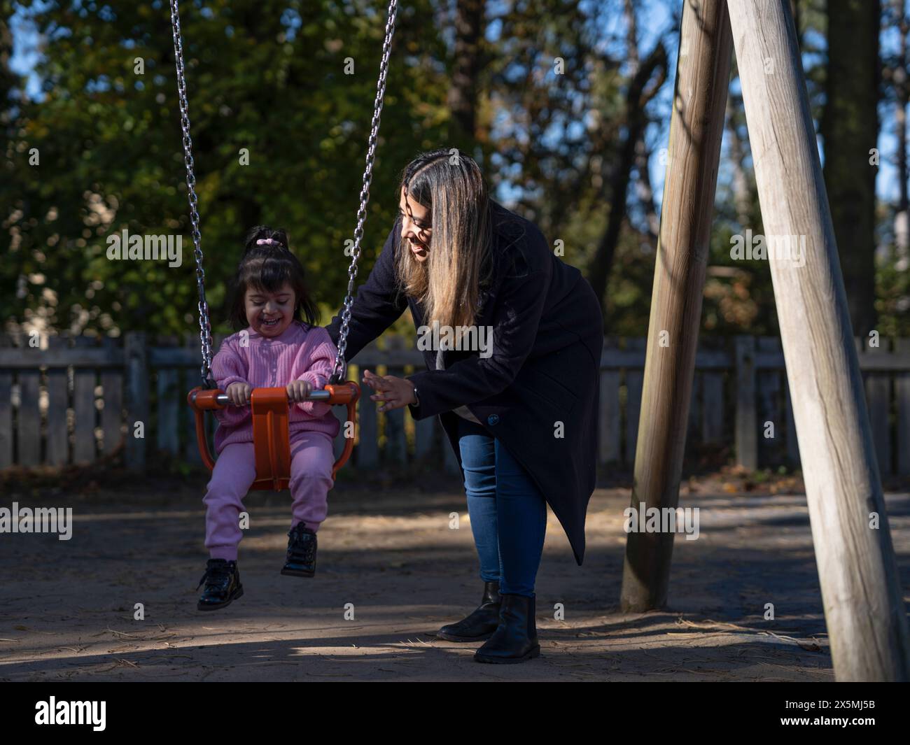 Mutter Schwingtochter mit Down-Syndrom auf Spielplatzschaukel Stockfoto