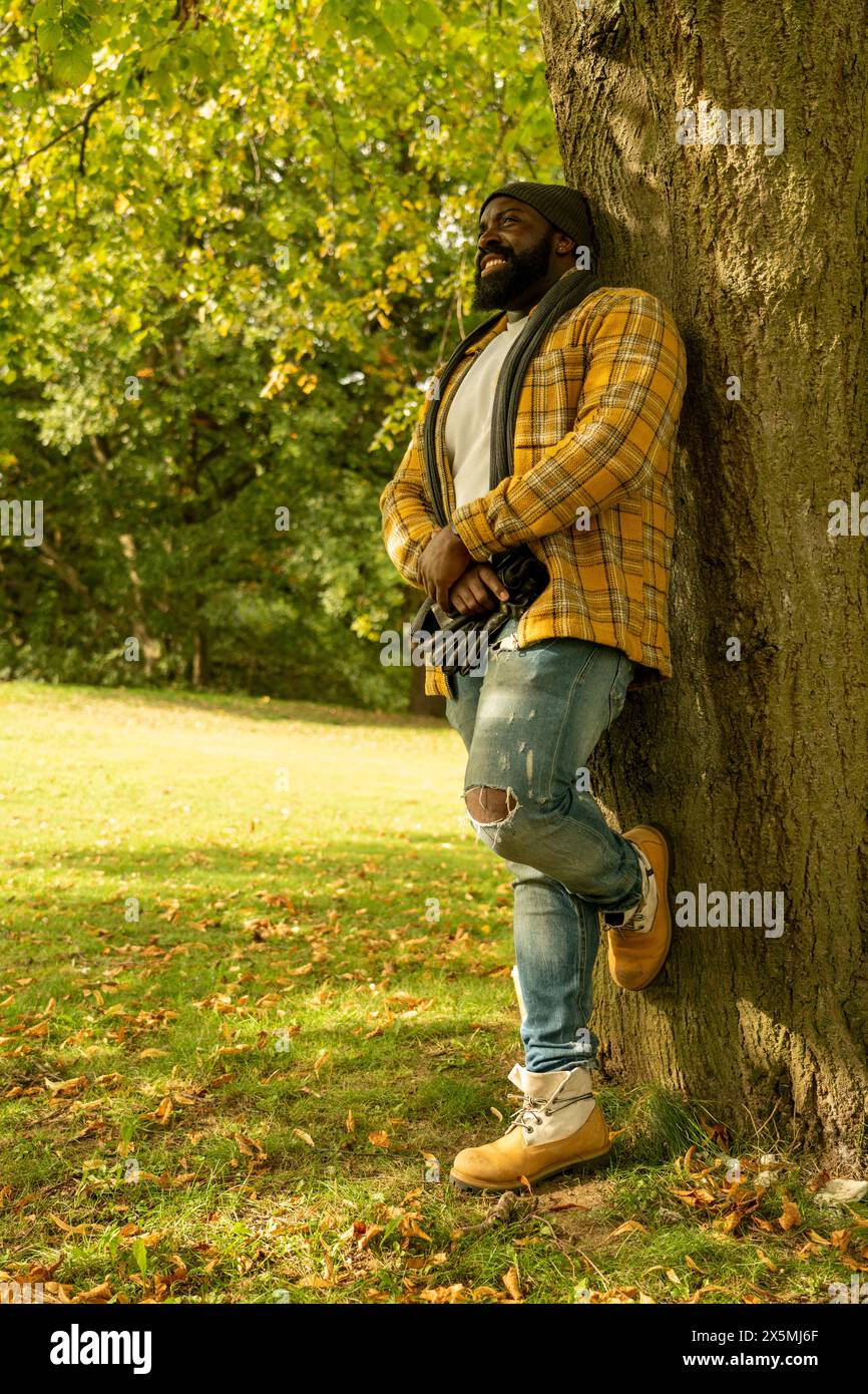 Lächelnder Mann, der sich im Herbst im Park auf Baumstamm lehnt Stockfoto