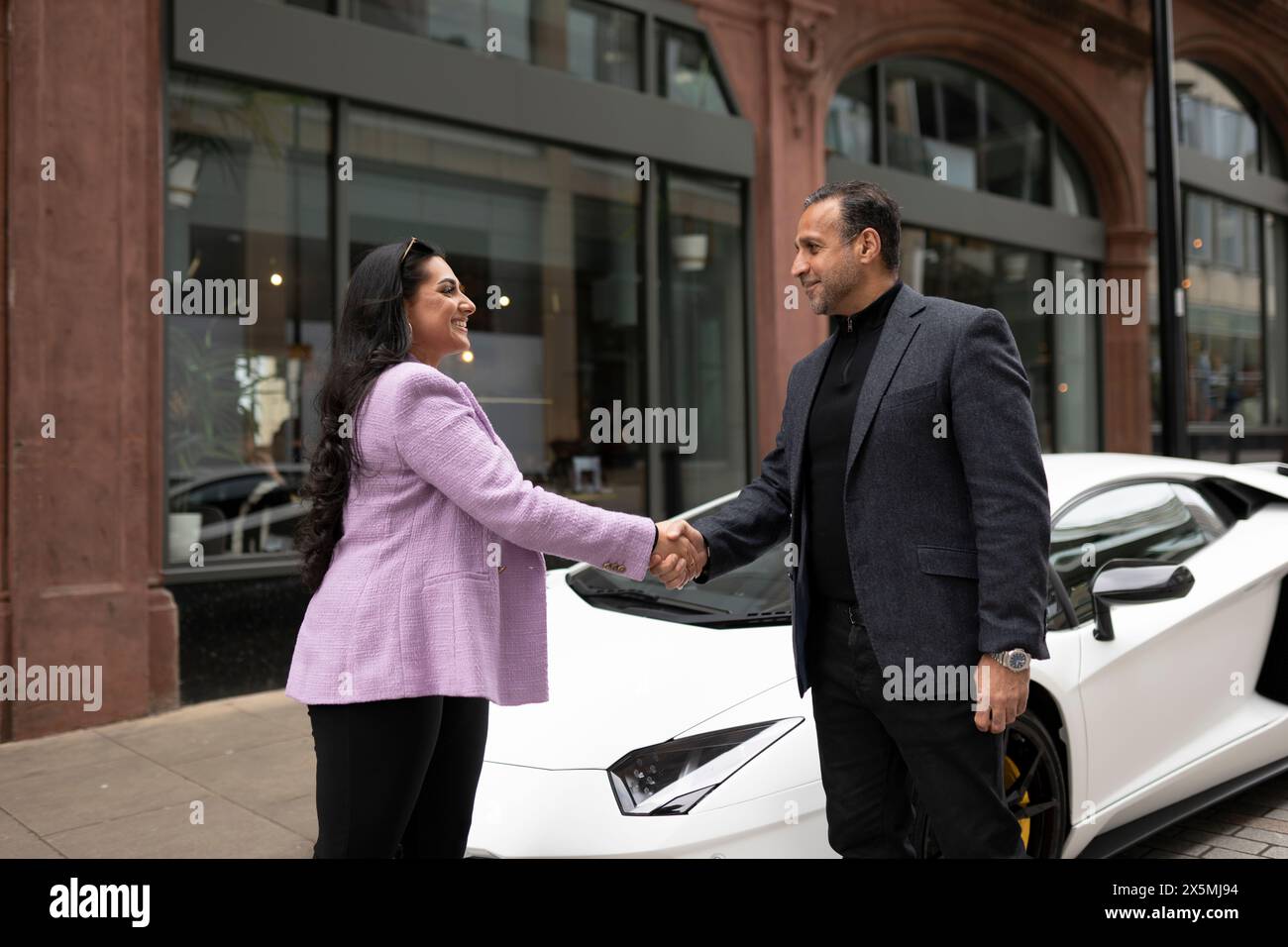 Geschäftspartner schütteln sich die Hände mit einem Luxuswagen Stockfoto