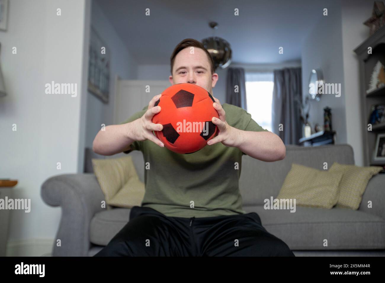 Porträt eines Mannes, der auf dem Sofa sitzt und Fußball hält Stockfoto