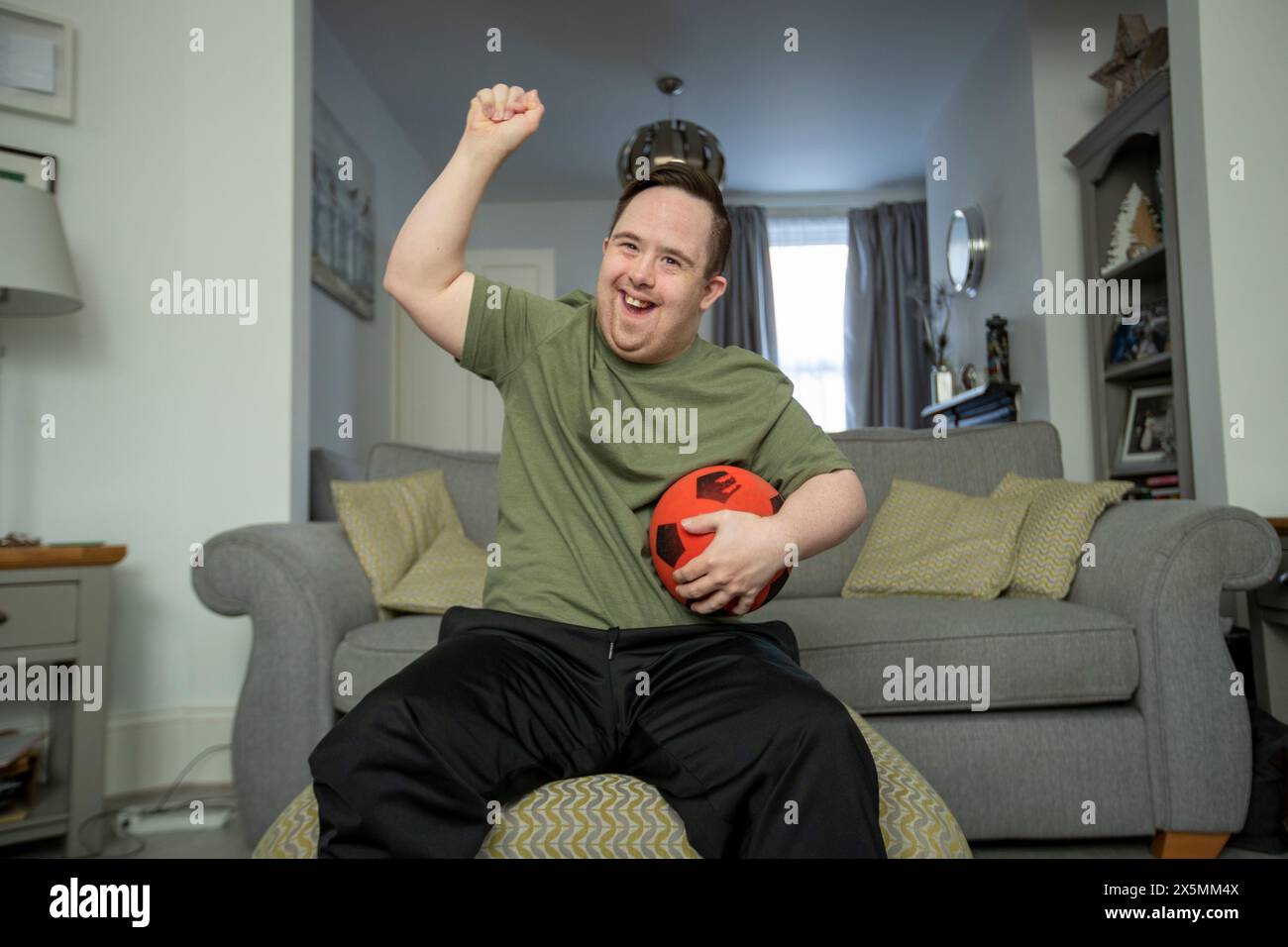 Mann sitzt auf dem Sofa, hält Fußball und jubelt Stockfoto
