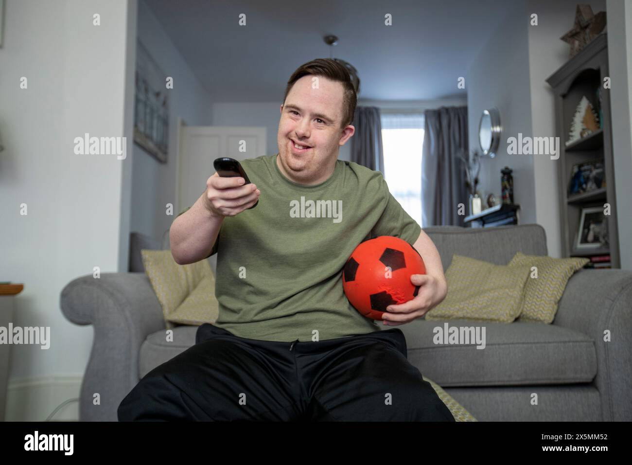 Mann, der auf dem Sofa sitzt, Fußball und Fernbedienung hält Stockfoto
