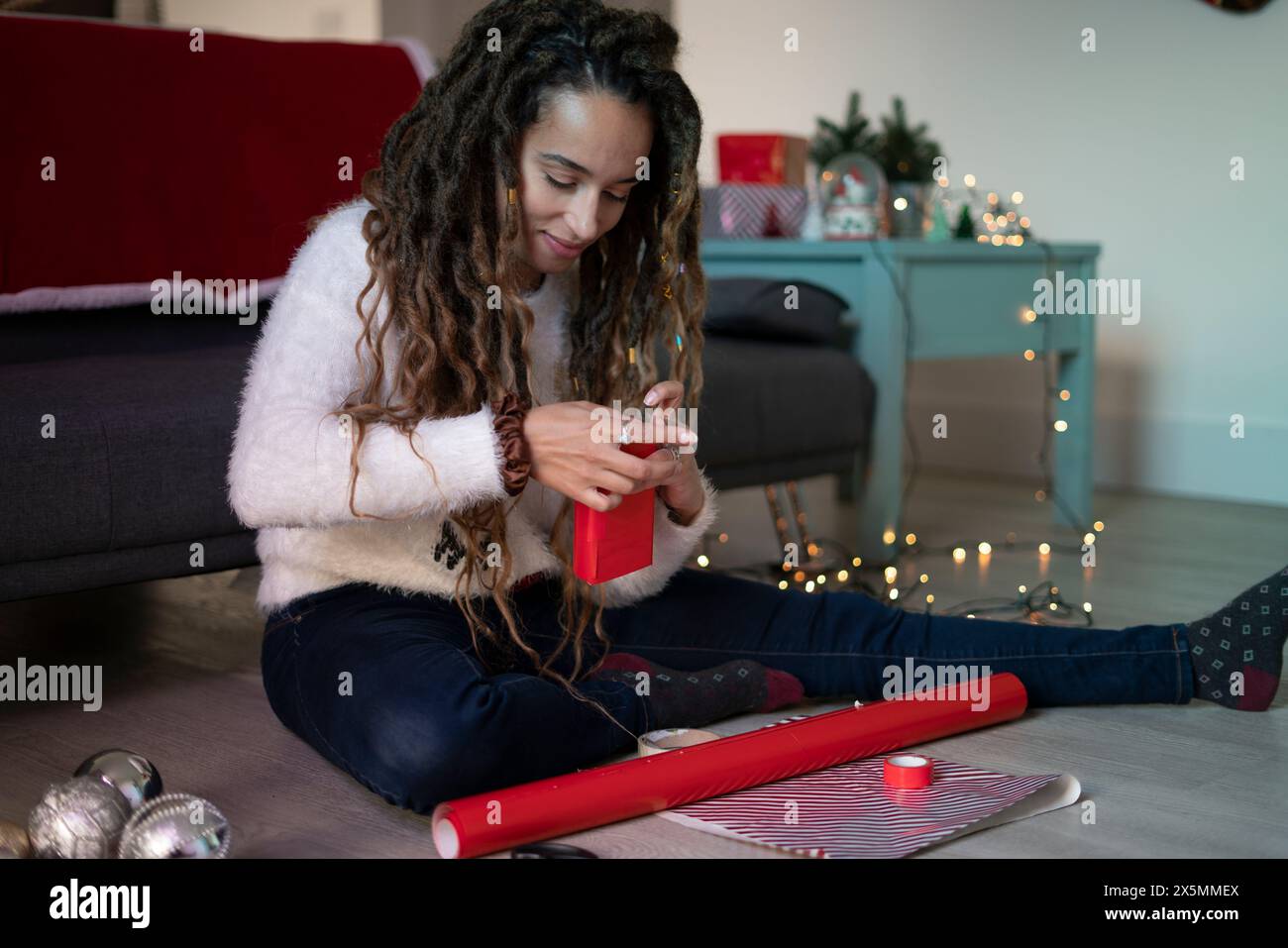 Frau, die auf dem Boden im Wohnzimmer sitzt und Weihnachtsvorstellungen vorbereitet Stockfoto