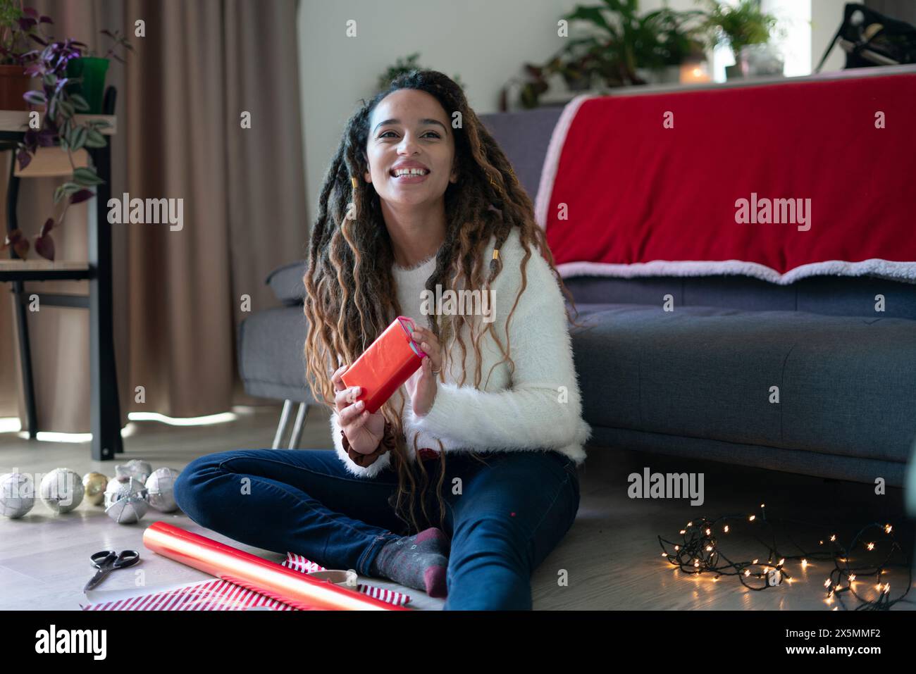 Frau, die auf dem Boden im Wohnzimmer sitzt und Weihnachtsvorstellungen vorbereitet Stockfoto