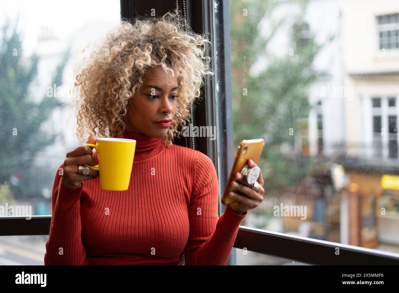 Frau, die einen Becher hält und ein Smartphone benutzt Stockfoto