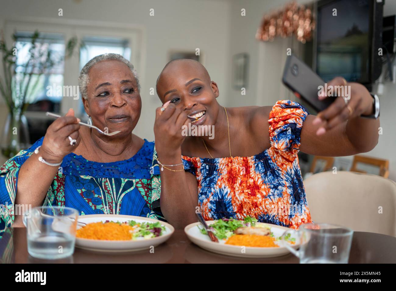 Lächelnde Seniorin mit erwachsener Tochter, die Abendessen isst und Selfie macht Stockfoto