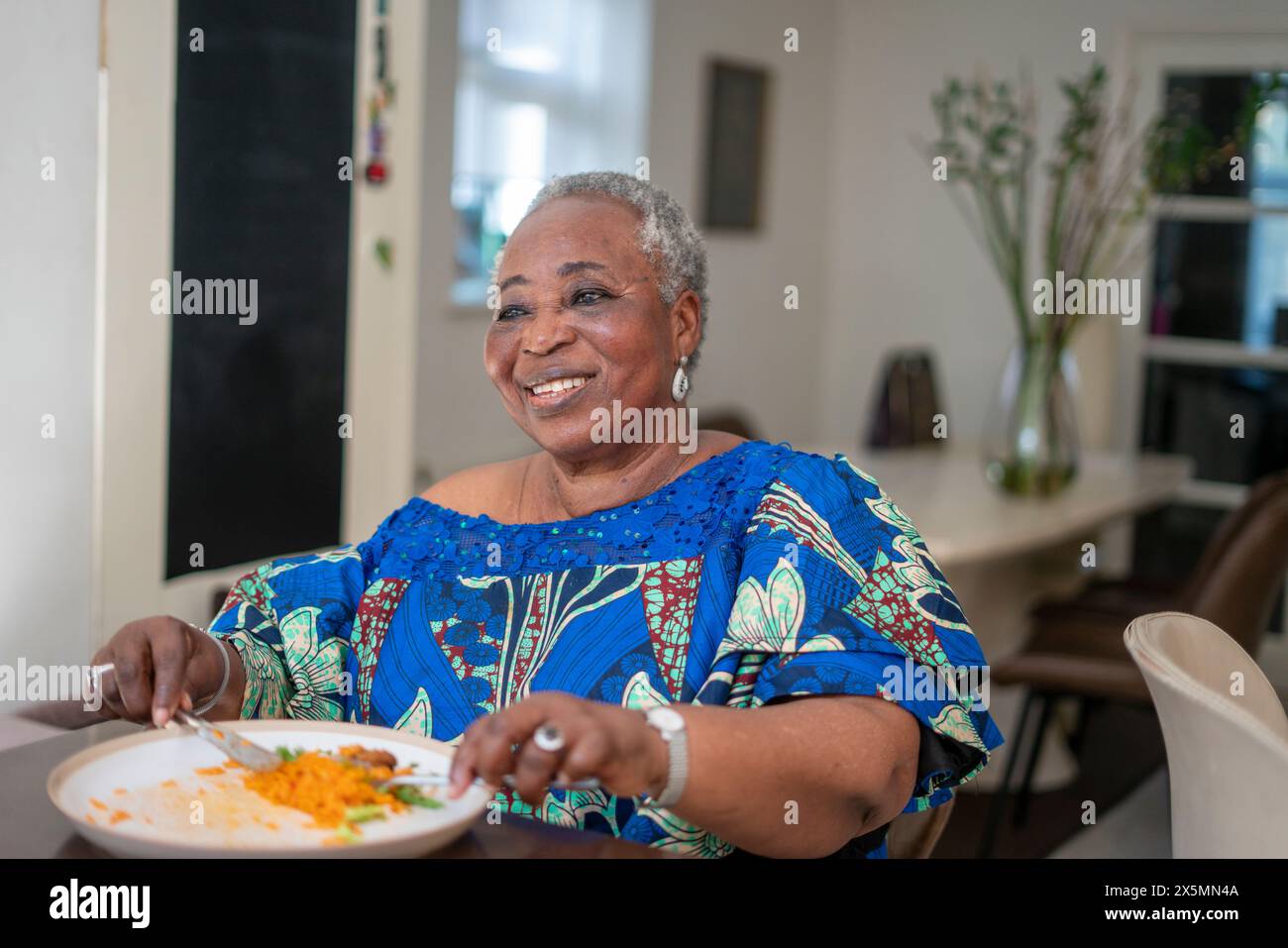 Lächelnde Seniorin, die zu Hause zu Abend isst Stockfoto