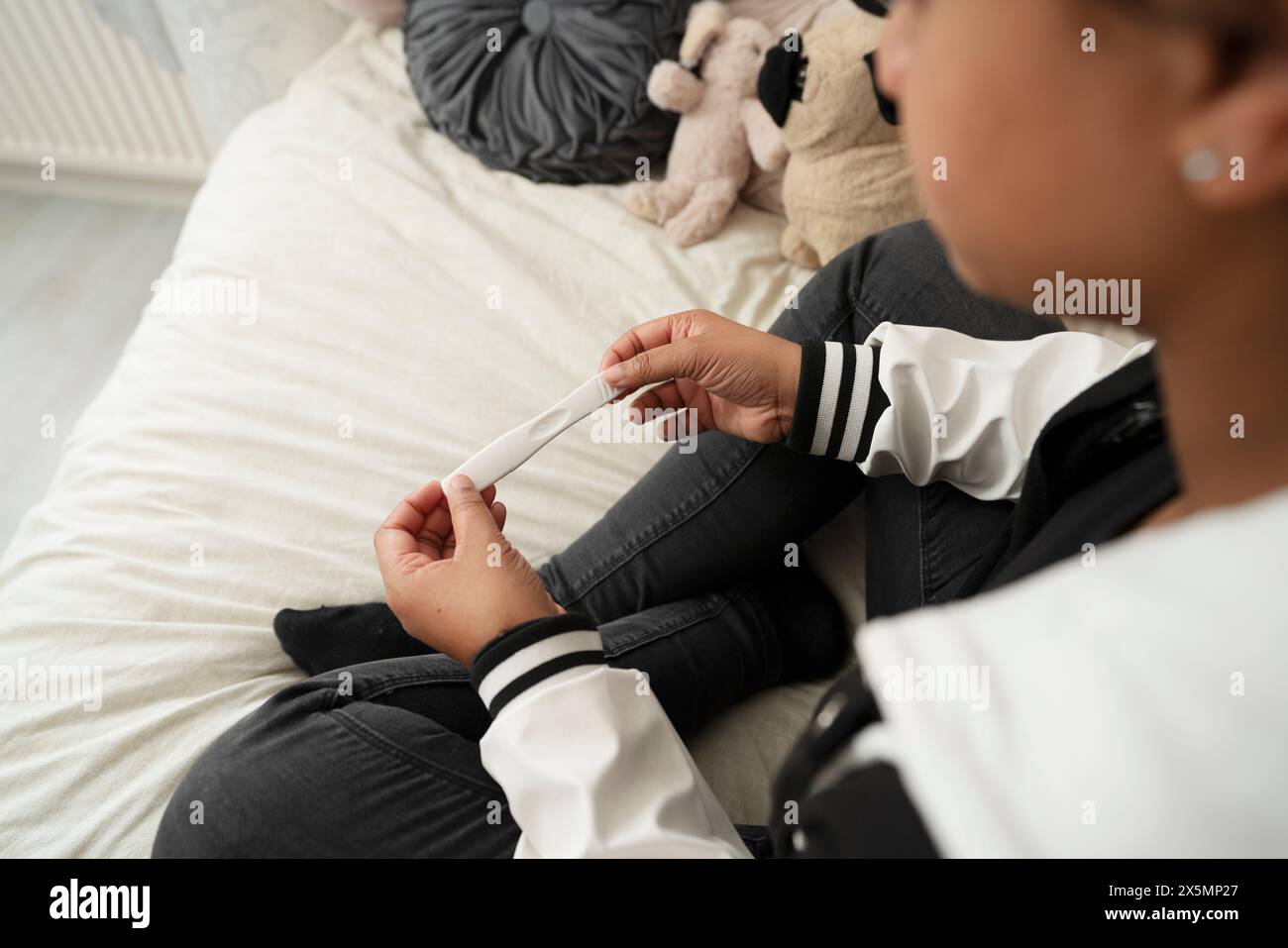 Mädchen, das auf dem Bett sitzt und einen Schwangerschaftstest hat Stockfoto