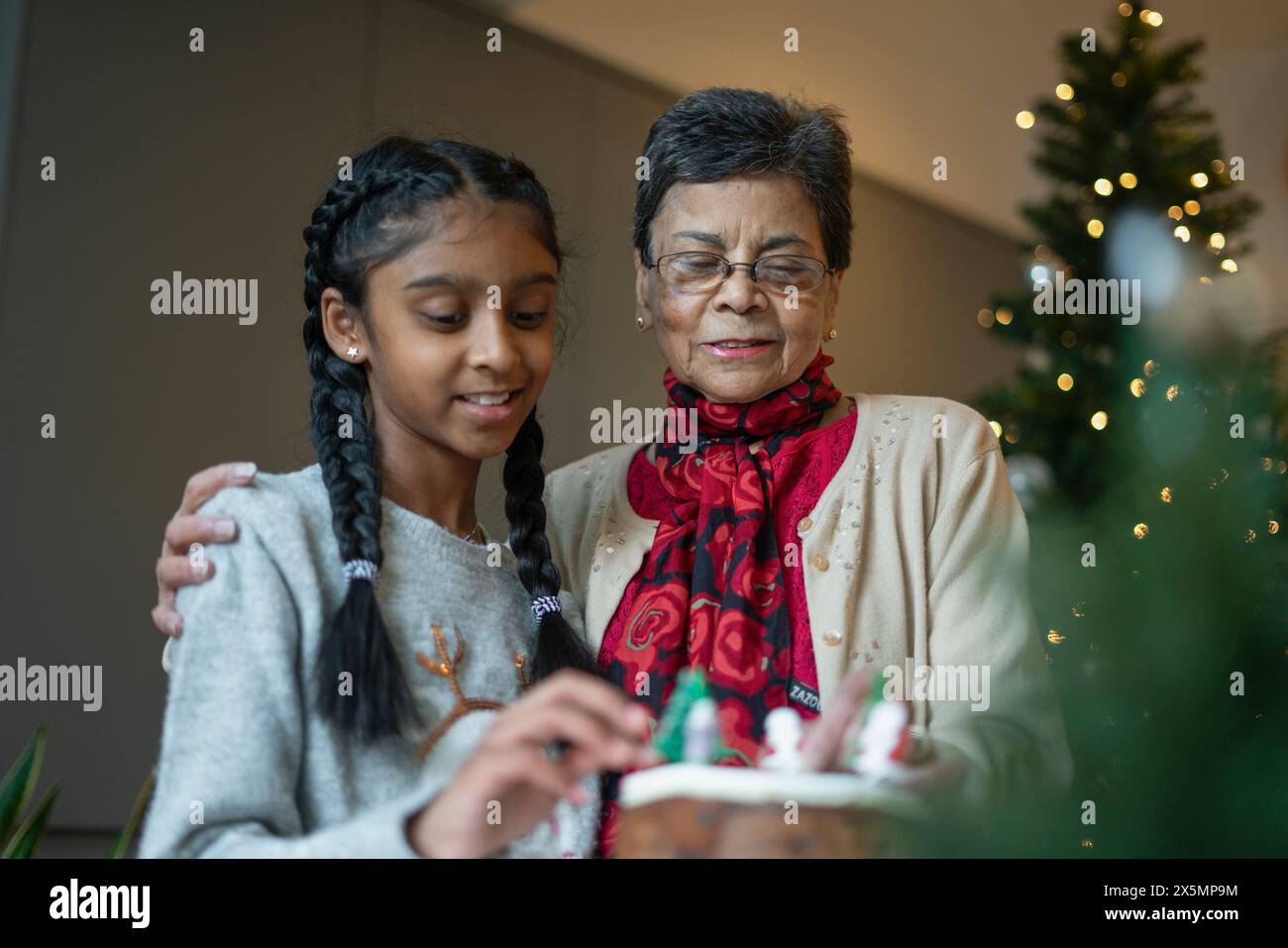 Lächelndes Mädchen mit Großmutter, die Weihnachtskuchen dekoriert Stockfoto