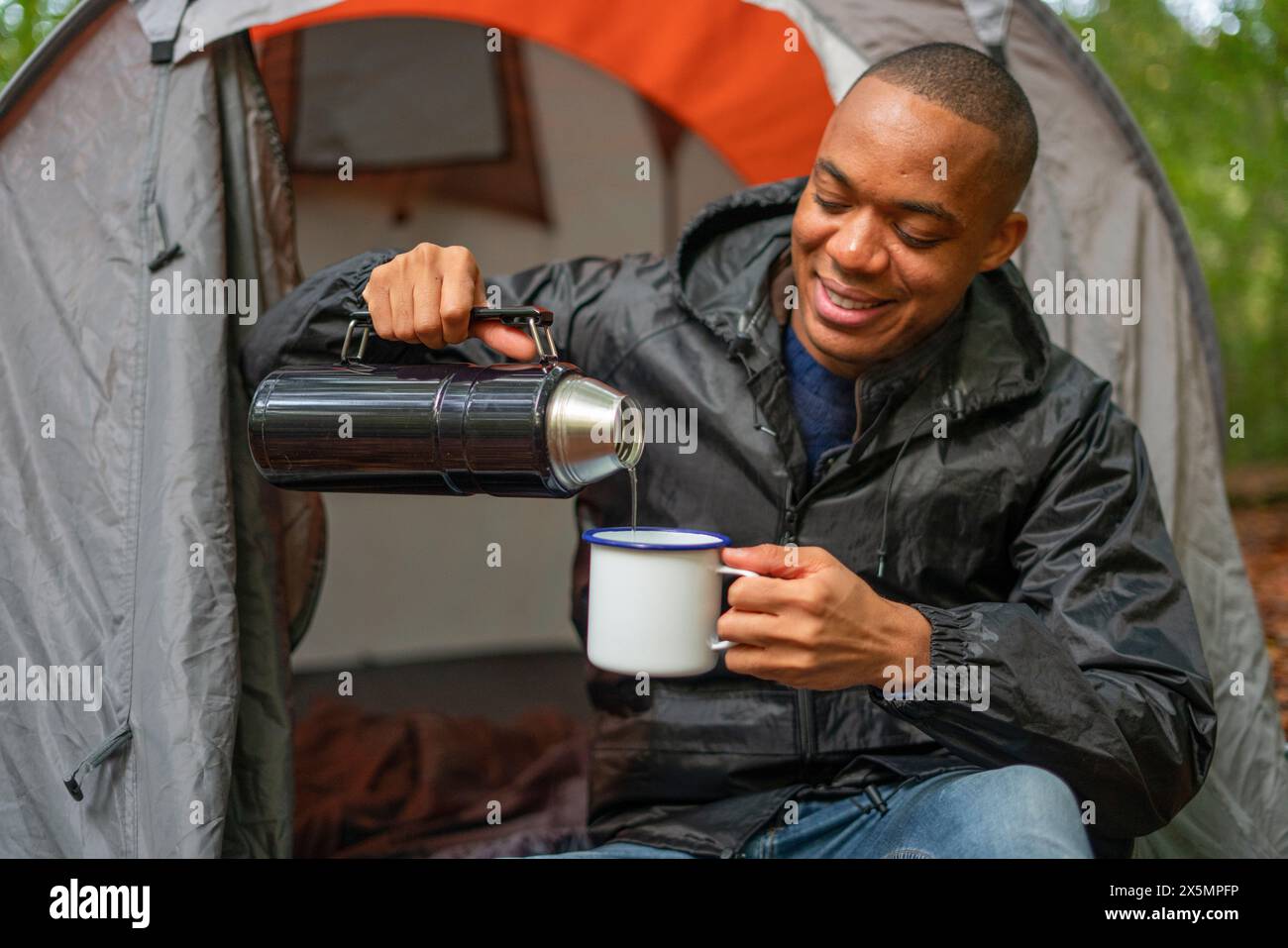 Mann, der vor dem Zelt sitzt und heißes Getränk gießt Stockfoto