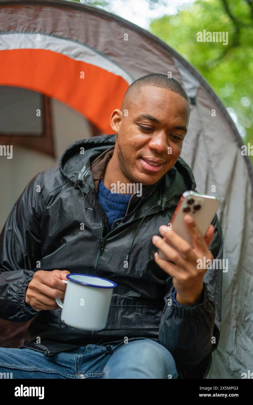 Mann, der vor dem Zelt sitzt und auf das Smartphone schaut Stockfoto