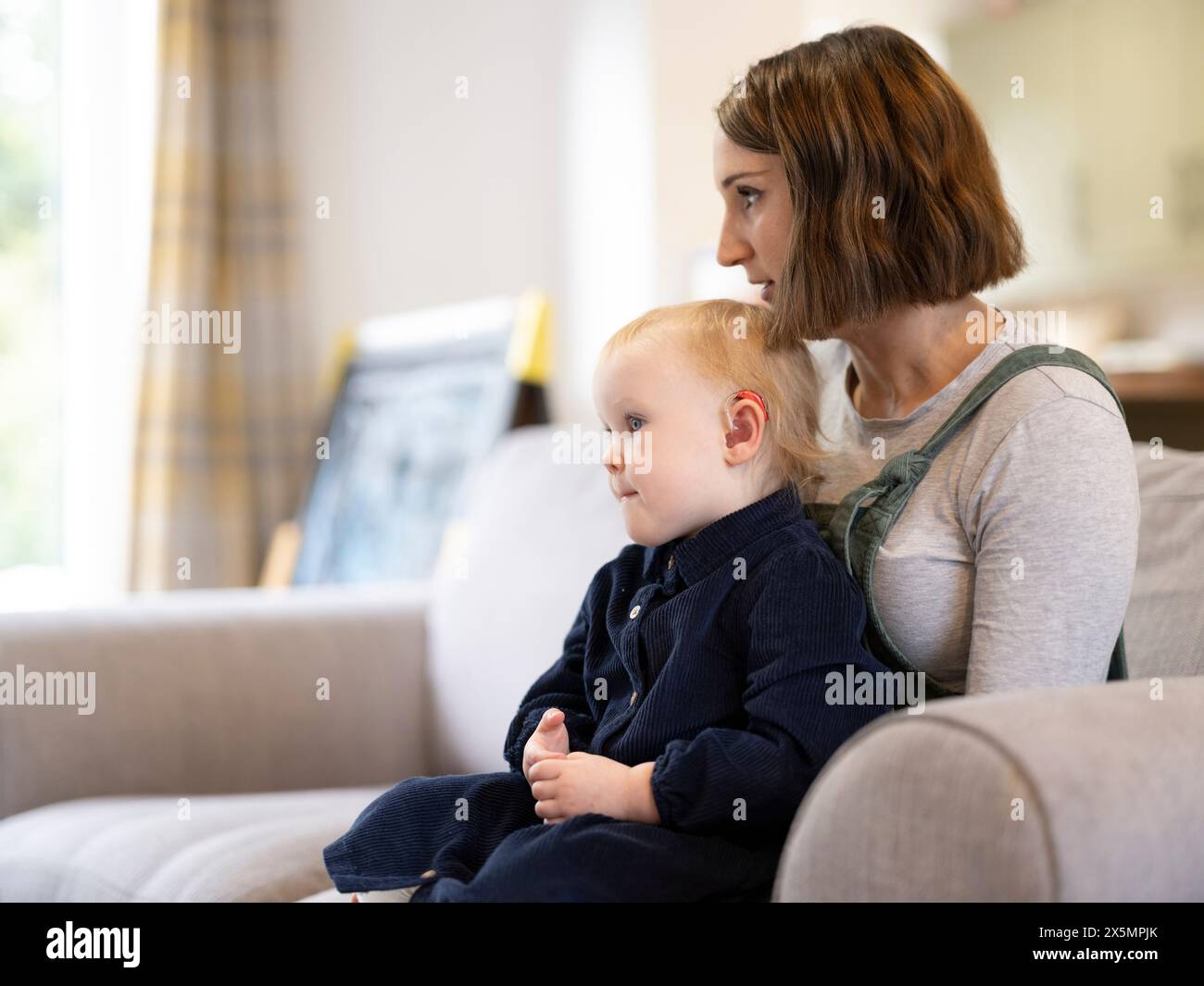 Tochter sitzt zu Hause auf dem Schoß der Mutter Stockfoto