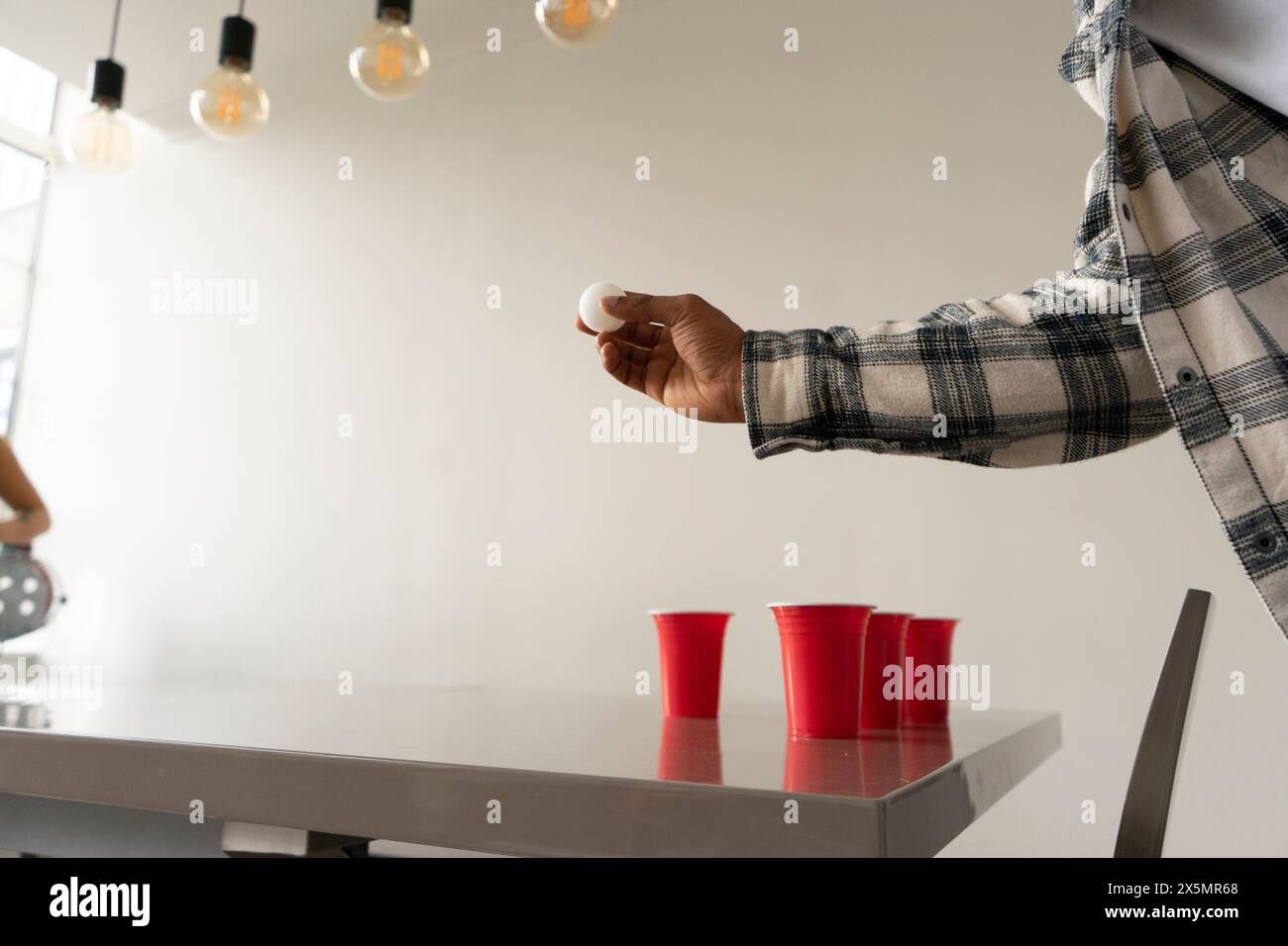 Ein Mann hält Tischtennisball, während er auf der Heimparty Bier Pong spielt Stockfoto