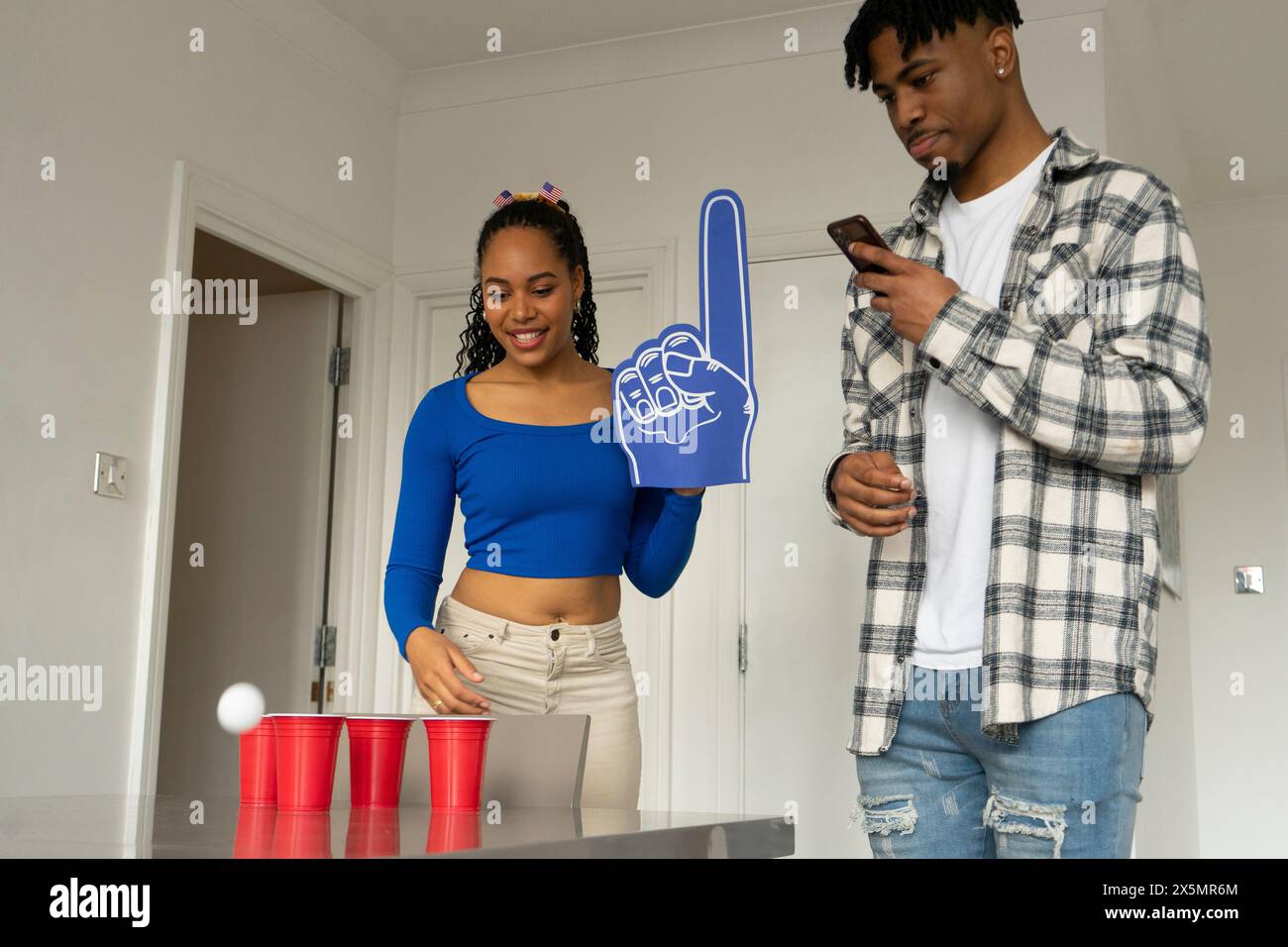 Frau jubelte und Mann benutzte Smartphone beim Bierpong zu Hause Stockfoto