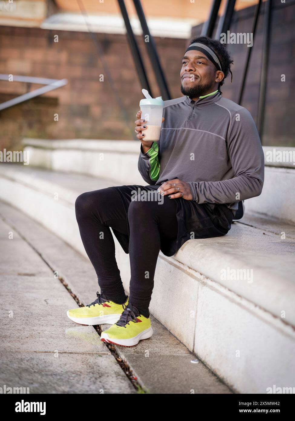 Sportlicher Mann mit Proteingetränk auf Stufen im Freien Stockfoto