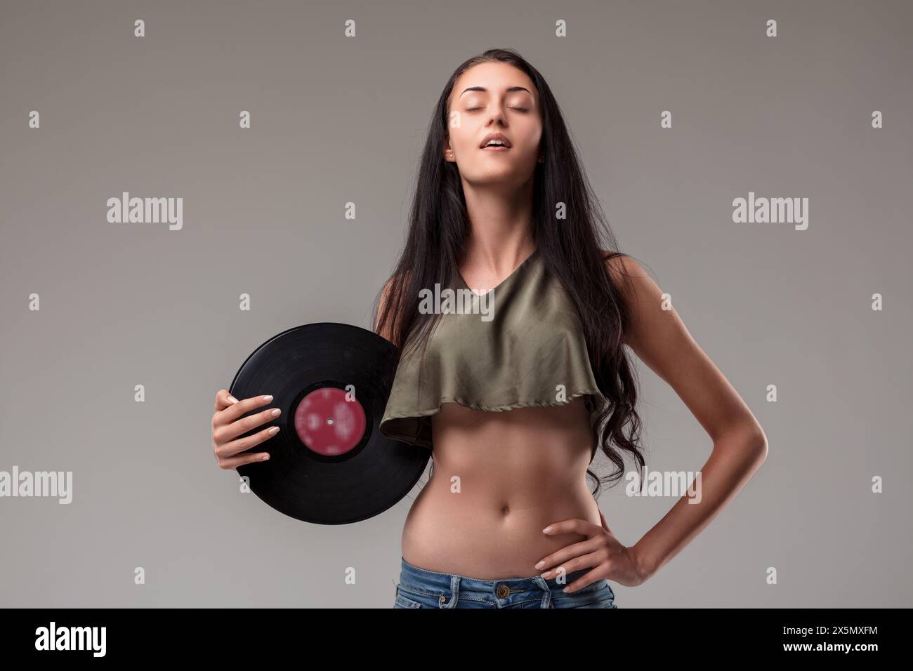 Stolze und ruhige junge Frau in grünem Top und Denim, die den Moment mit einer klassischen Schallplatte in der Hand genießt Stockfoto