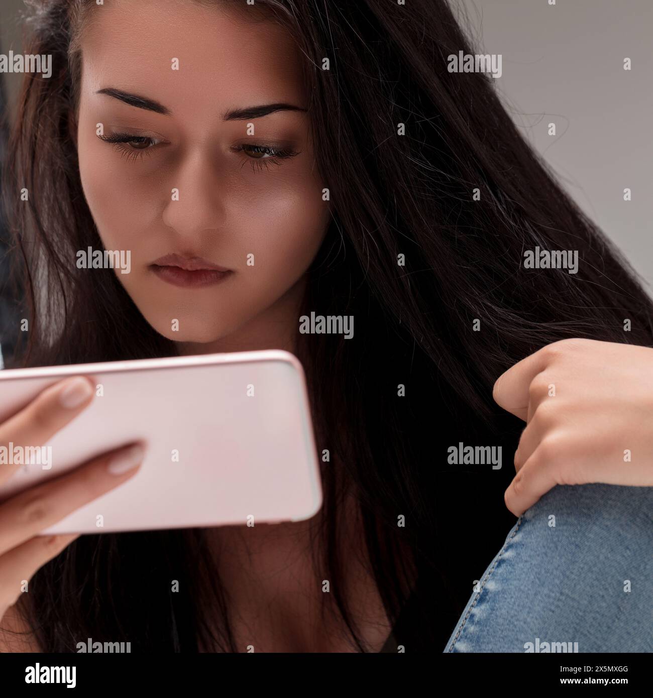 Der Blick der jungen Frau ist fest auf ihrem Handy und spiegelt einen Moment der persönlichen Reflexion und der digitalen Interaktion wider Stockfoto