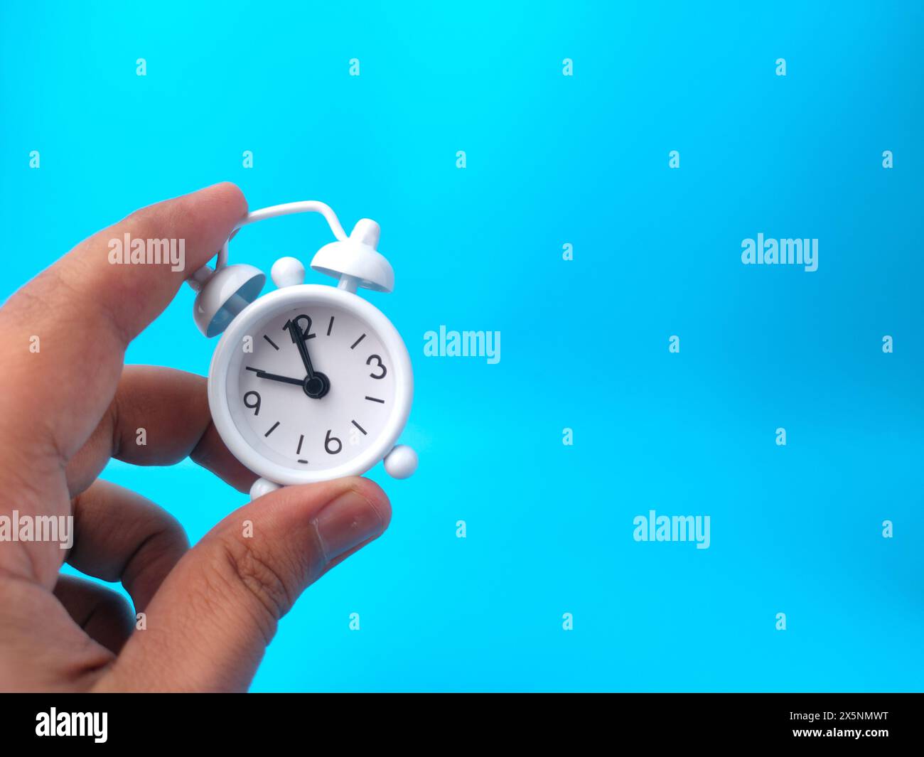 Hand mit weißem Wecker auf blauem Hintergrund und Kopierraum. Stockfoto