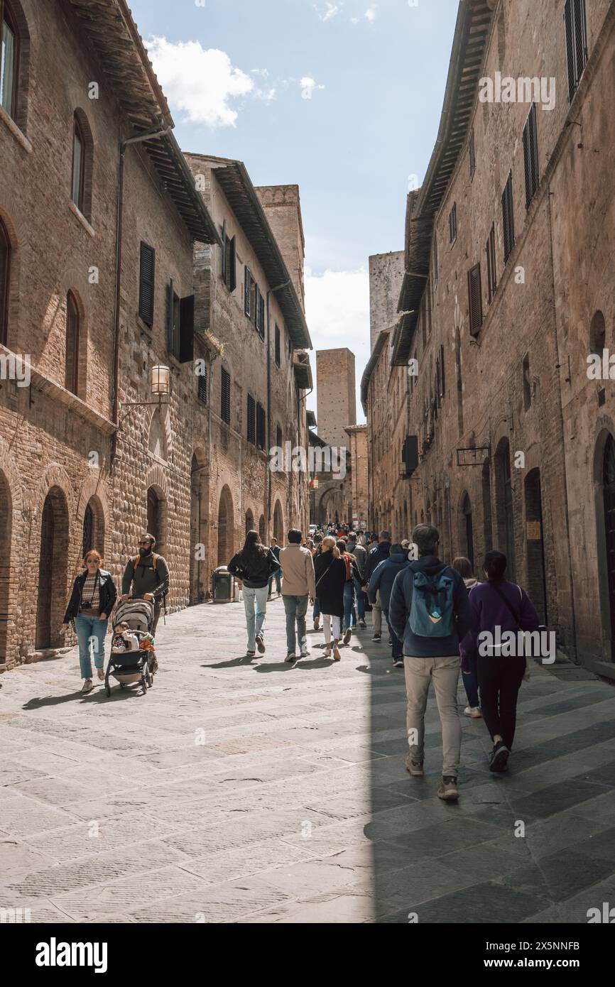 Touristen, die an einem schönen sonnigen Tag auf einer belebten Straße im Zentrum der historischen mittelalterlichen Stadt San Gimignano in der Toskana spazieren gehen. Stockfoto
