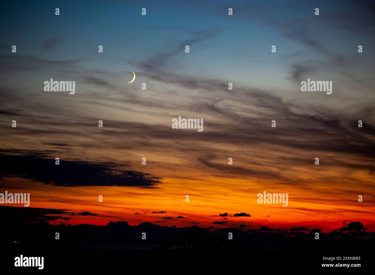 Rot-oranger Himmel bei Sonnenuntergang am Abenddämmerabend mit dunklen Wolken und Mond. Naturhimmel. Hintergrund, Horizont goldener Himmel, Sonnenaufgangswolke herrlich. Stockfoto