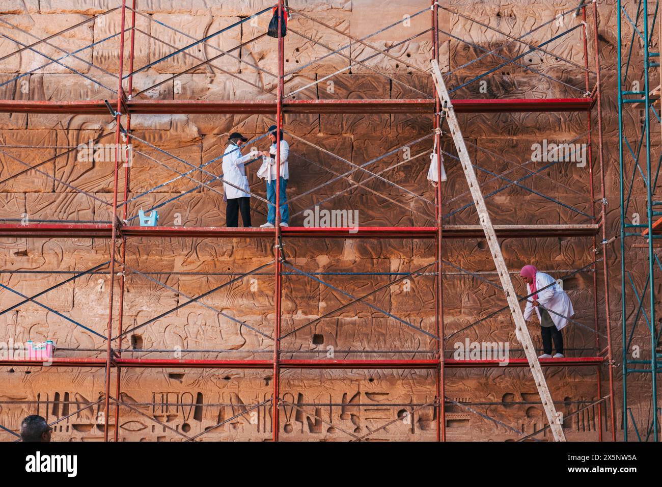 Arbeiter in Labormänteln auf Gerüsten arbeiten an der Restaurierung und Erhaltung der Steinmauern des Tempels in Medinet Habu in Luxor, Ägypten Stockfoto