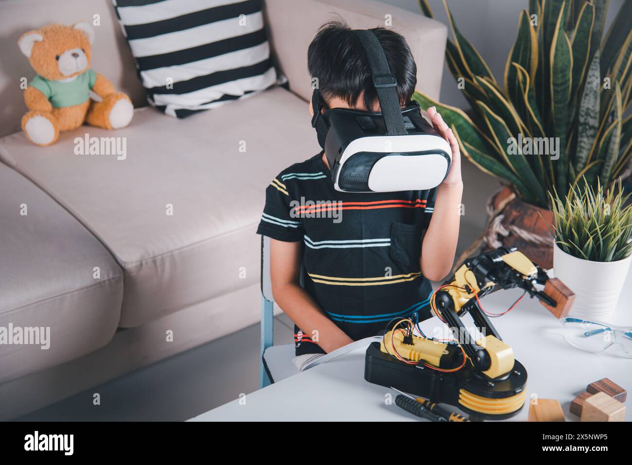 Asiatischer Junge mit VR-Brille auf Roboterarm in der Werkstatt Stockfoto