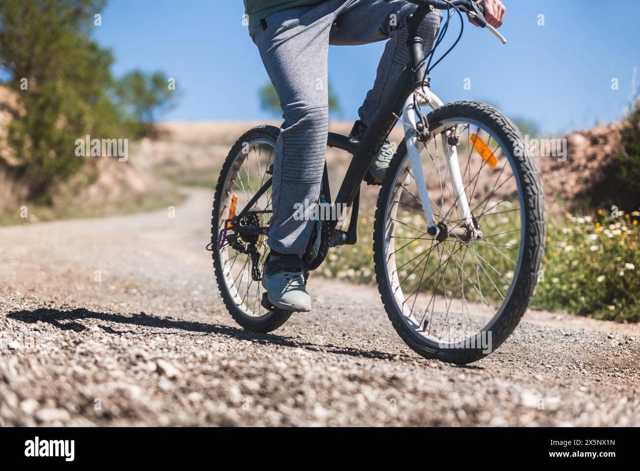 Eine Person fährt mit dem Fahrrad auf einer Feldstraße. Das Motorrad ist schwarz-weiß. Der Reiter trägt graue Hosen Stockfoto