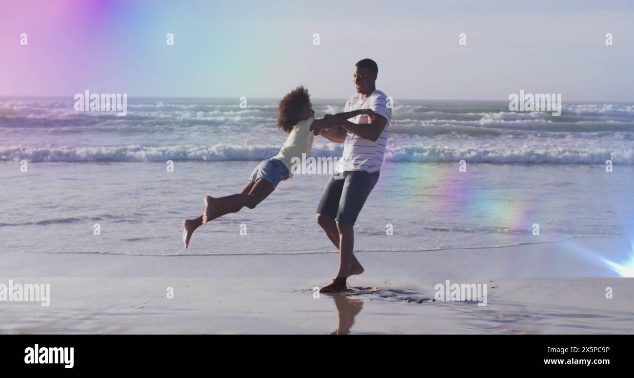 Bild von Lichtflecken über dem afroamerikanischen Vater mit Tochter am Strand Stockfoto