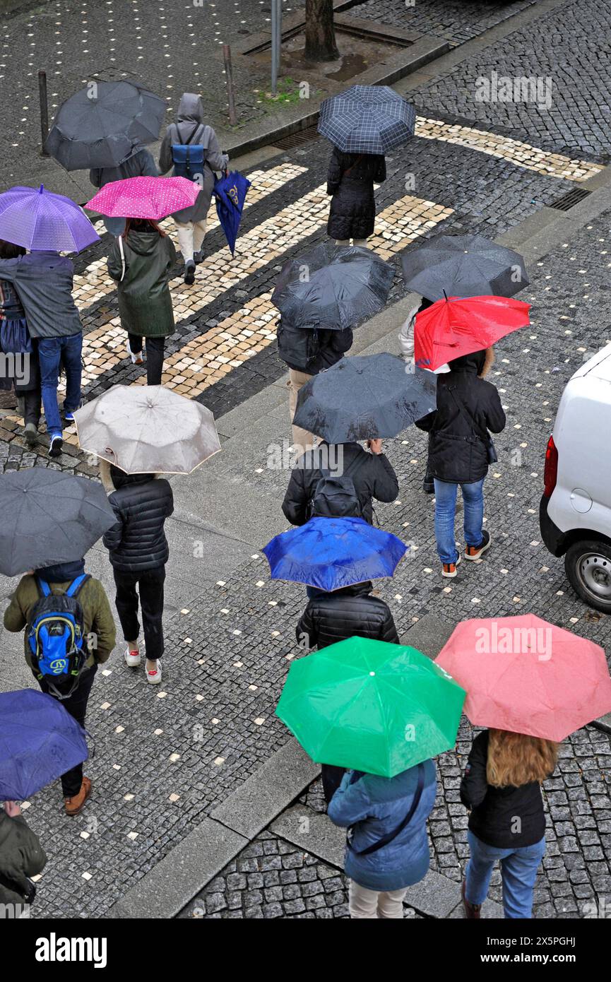 Menschen, die an einem regnerischen Tag in Porto, Portugal, Europa eine Straße mit bunten Regenschirmen überqueren Stockfoto
