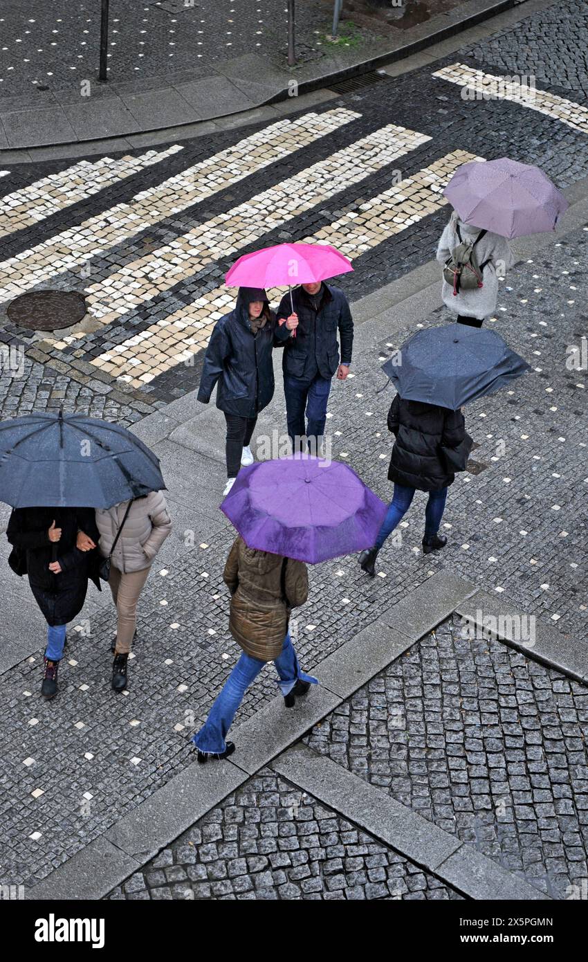 Menschen, die an einem regnerischen Tag in Porto, Portugal, Europa eine Straße mit bunten Regenschirmen überqueren Stockfoto
