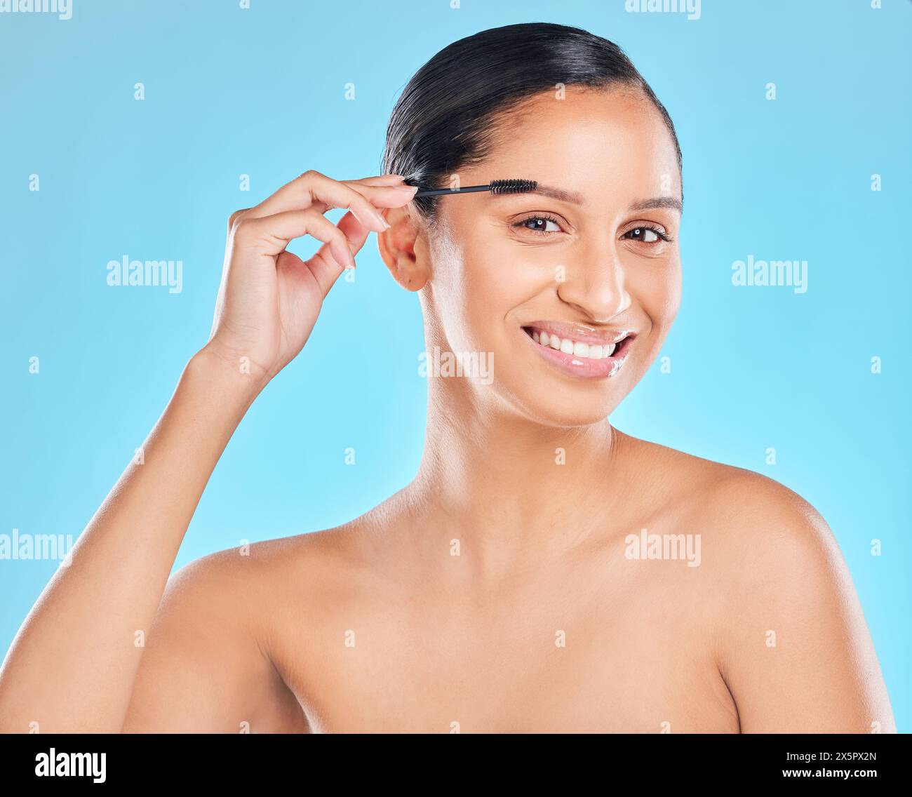 Porträt, Schönheit und glückliche Frau mit Mascara-Bürste für Glanz, Glanz oder Hautpflege isoliert auf blauem Studiohintergrund. Gesicht, Make-up und Augenbraue auftragen Stockfoto