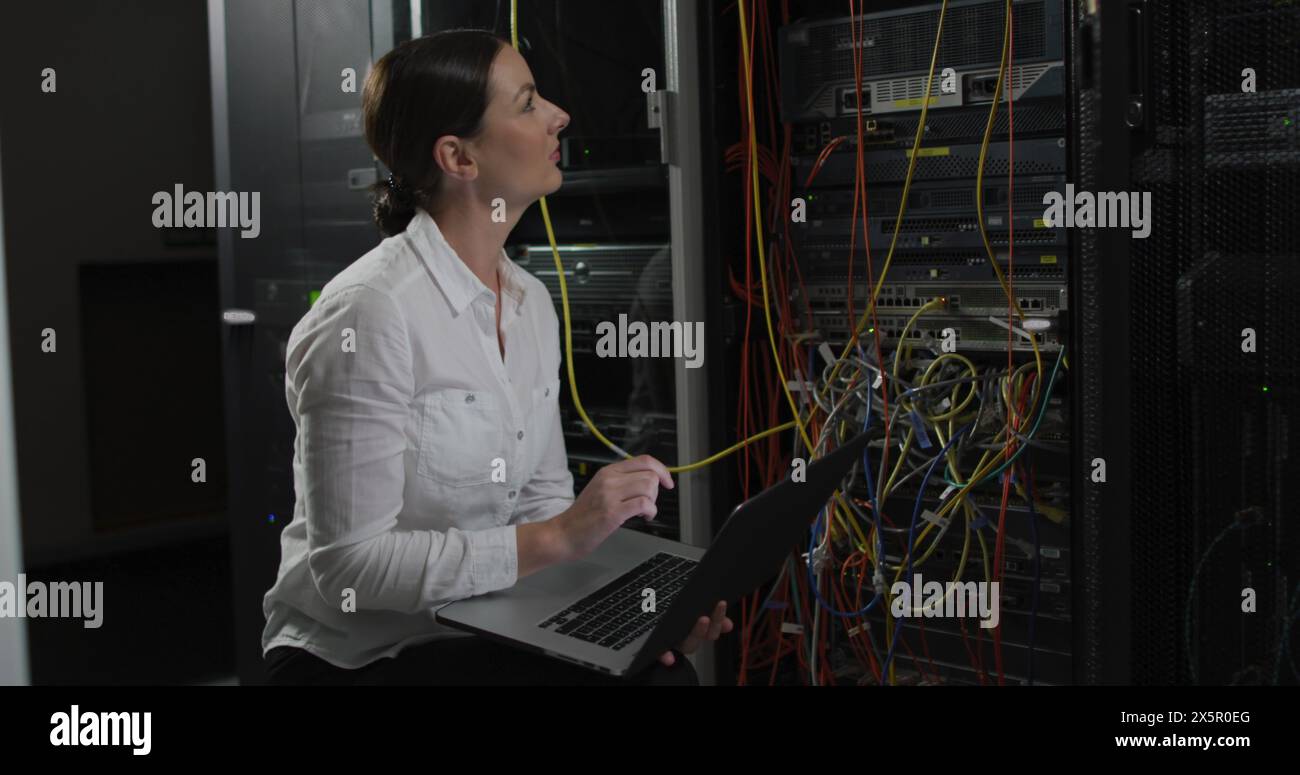 Kaukasierin, die einen Laptop hält, im Serverraum arbeitet Stockfoto