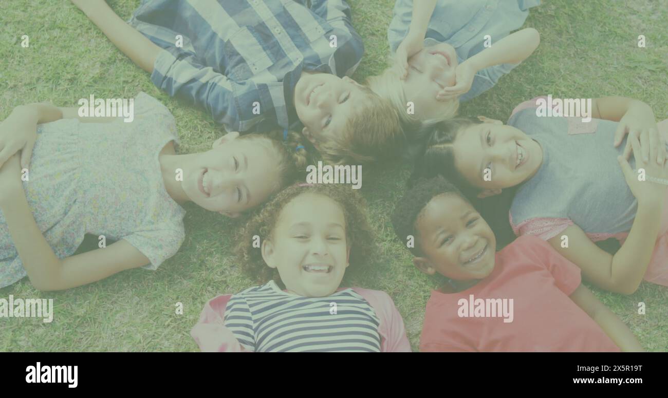 Schulkinder liegen auf Gras, lachen und schauen in die Kamera Stockfoto