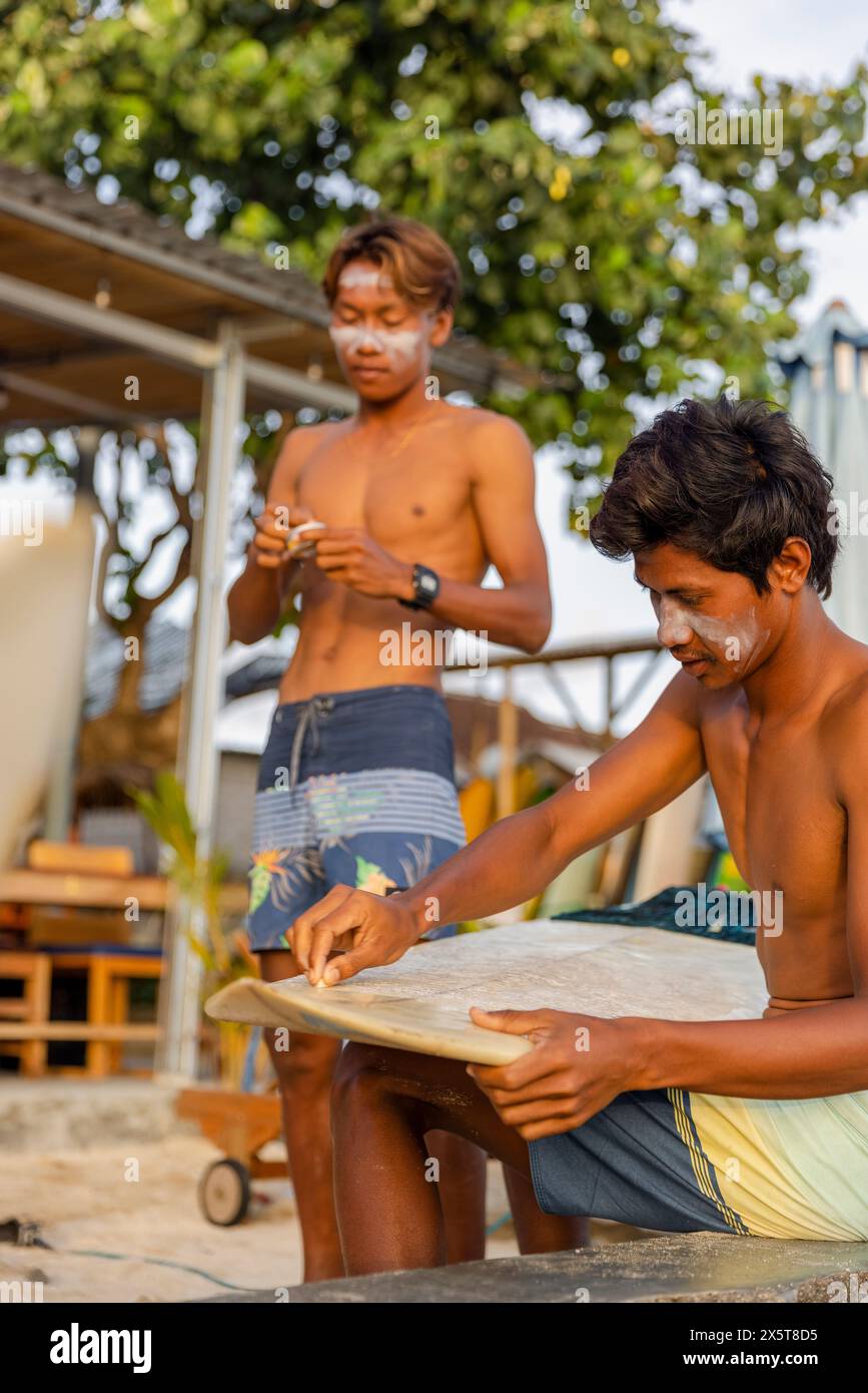 Surfer reinigen das Surfbrett und tragen am Strand Sonnencreme auf das Gesicht auf Stockfoto