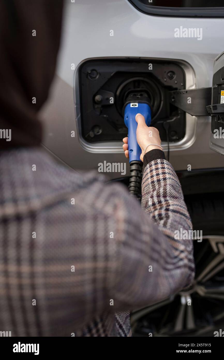 Frau, die Elektroauto auflädt, über die Schulter Stockfoto