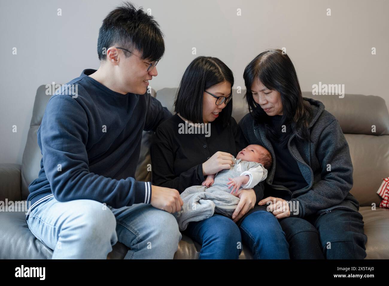 Familie in zwei Generationen mit Baby (0-1 Monate), das auf dem Sofa sitzt Stockfoto