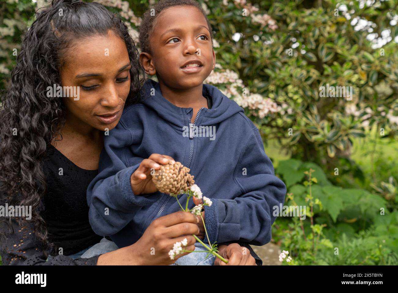 Mutter und Sohn halten Blumen und Kiefernzapfen Stockfoto