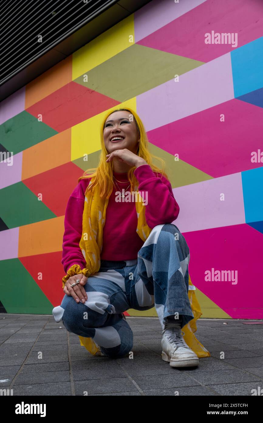 Junge Frau mit gelbem Haar, die draußen hockt Stockfoto