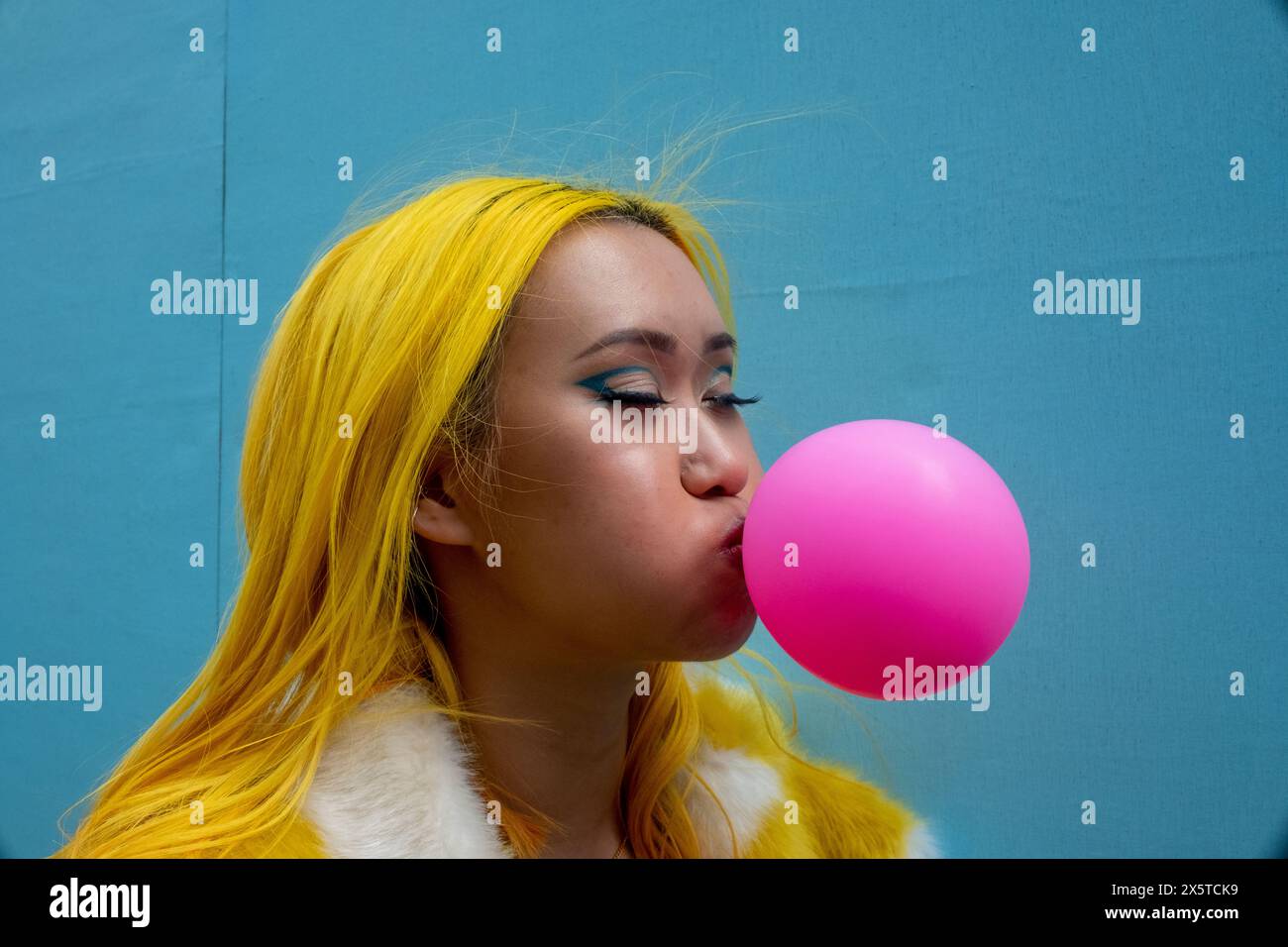 Eine junge Frau mit gelben Haaren, die Kaugummi bläst Stockfoto