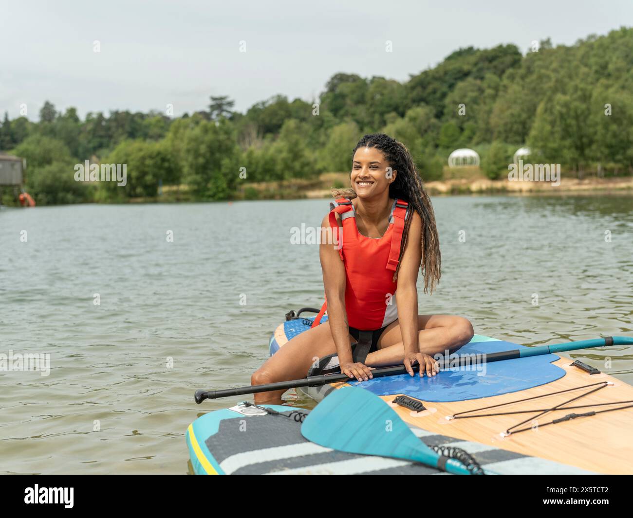 Lächelnde Frau, die auf dem Paddleboard auf dem See sitzt Stockfoto