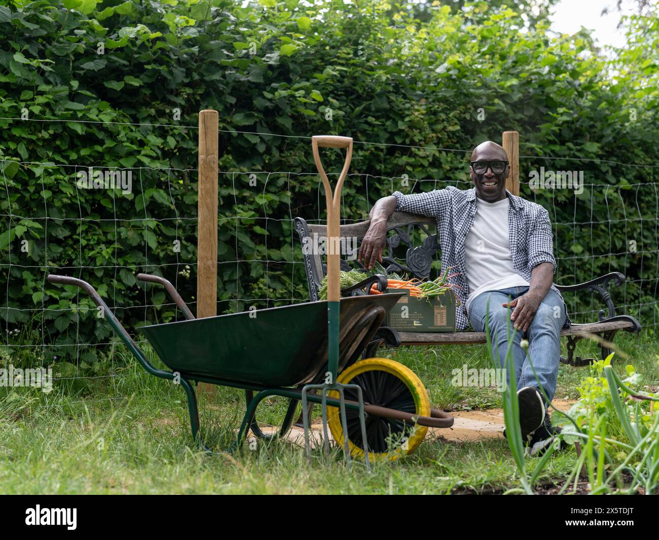 Ein lächelnder reifer Mann, der sich nach der Gartenarbeit auf der Bank ruht Stockfoto