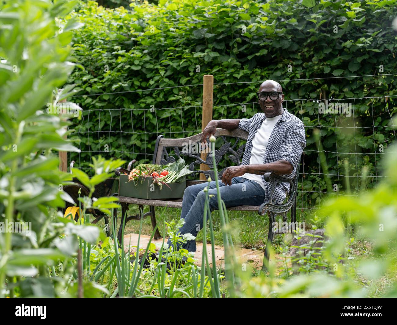 Ein lächelnder reifer Mann, der sich nach der Gartenarbeit auf der Bank ruht Stockfoto