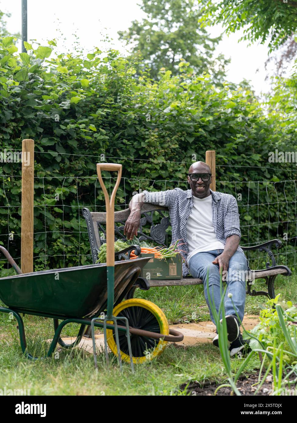 Ein lächelnder reifer Mann, der sich nach der Gartenarbeit auf der Bank ruht Stockfoto