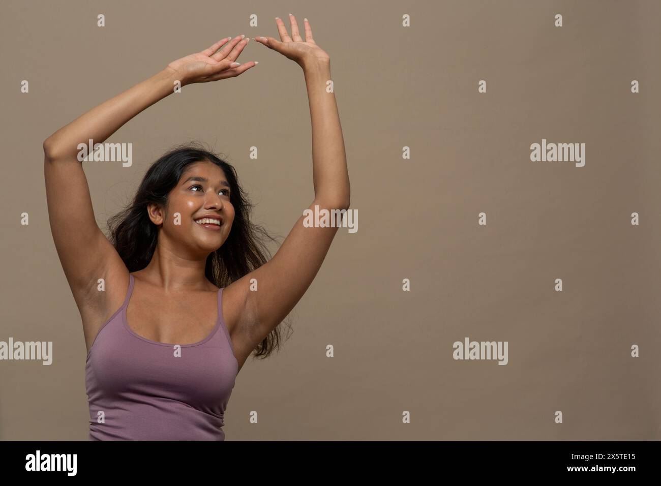Studio-Aufnahme einer lächelnden Frau in lila Oberseite mit erhobenen Armen Stockfoto