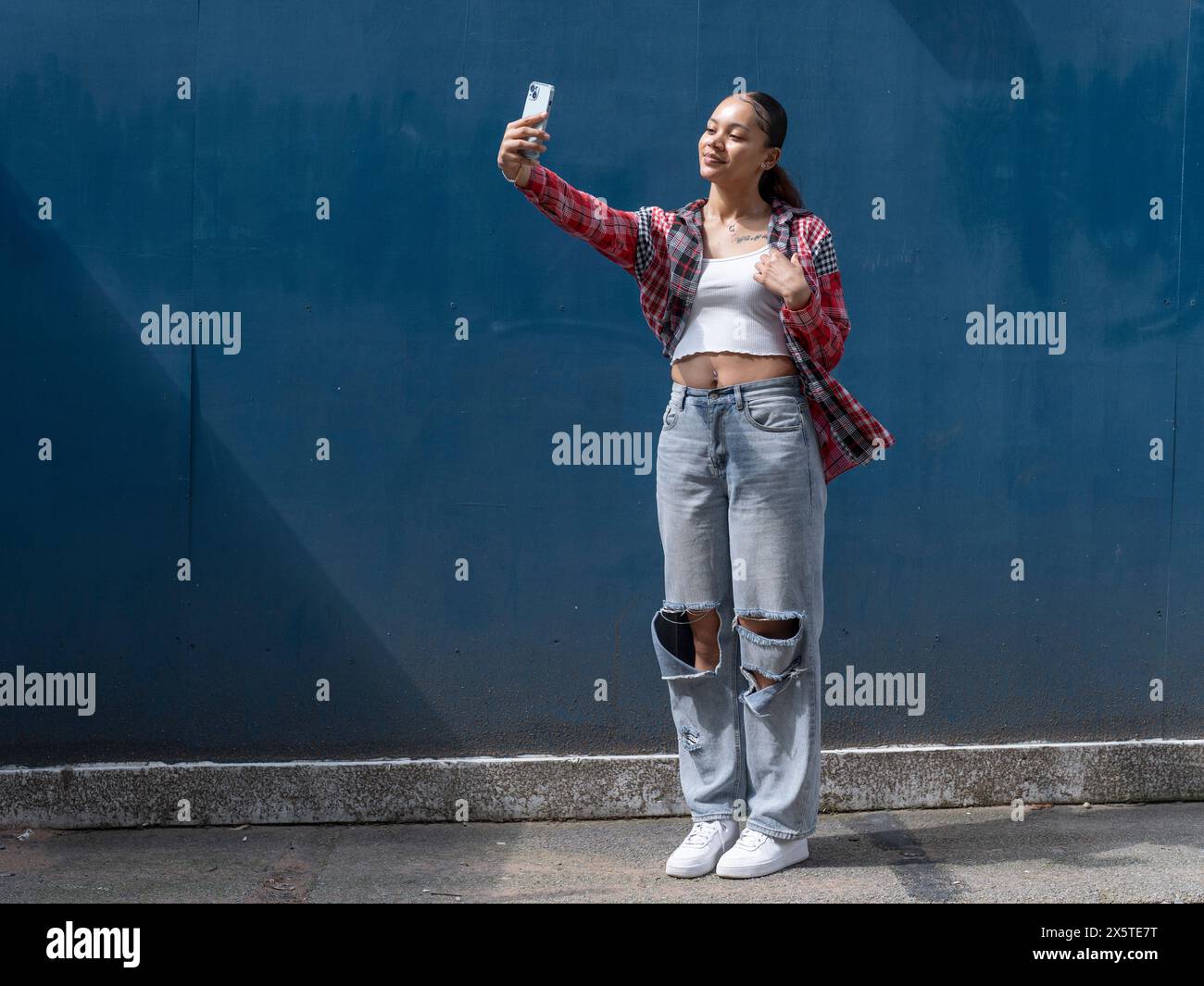 Eine junge Frau macht Selfie gegen die blaue Wand Stockfoto
