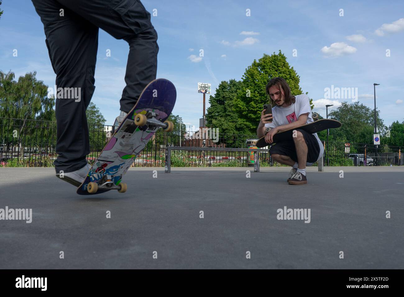 Ein Mann nimmt einen Freund auf, der Skateboard-Tricks macht Stockfoto