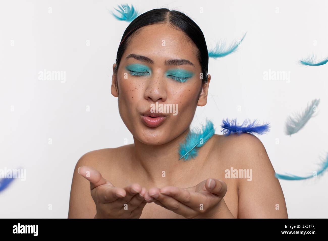 Frau mit blauem Make-up, das auf blauen Federn bläst Stockfoto