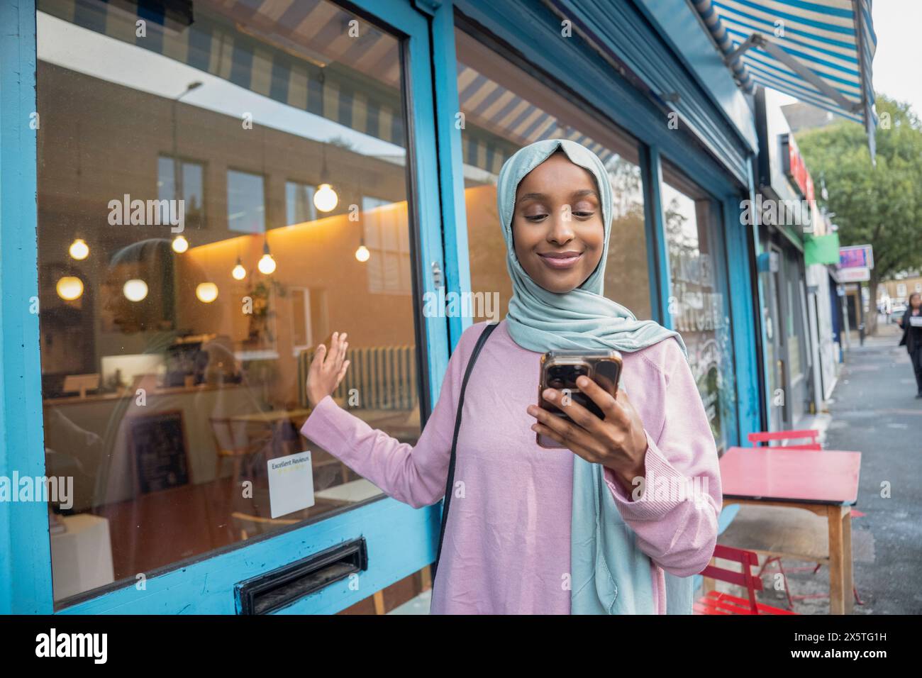 Eine junge Frau im Hijab, die vor dem Café telefoniert Stockfoto