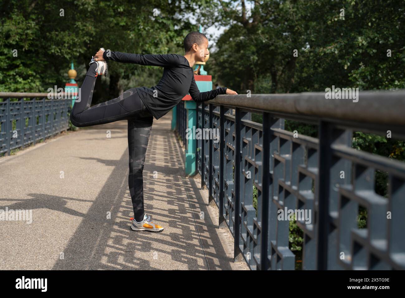 Sportliche Frau, die das Bein auf dem Steg im Park streckt Stockfoto