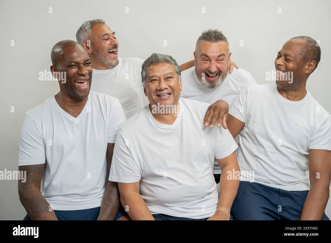 Gruppenporträt von älteren Männern in weißen T-Shirts, die vor grauem Hintergrund lachen Stockfoto